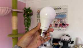 switchbot smart light bulb being held up in front of pink background