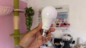 switchbot smart light bulb being held up in front of pink background