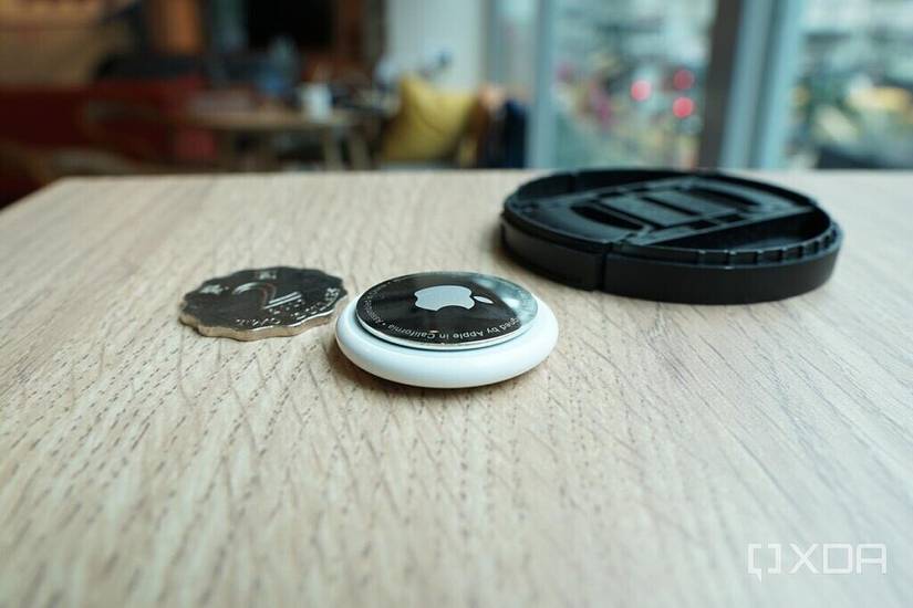 An AirTag with a Hong Kong coin and a camera lens lid.