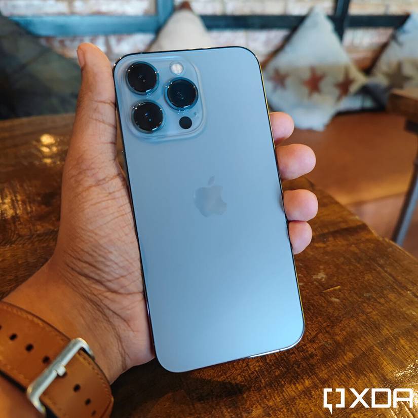Apple iPhone 13 Pro Sierra Blue held out in hand, over a wooden table