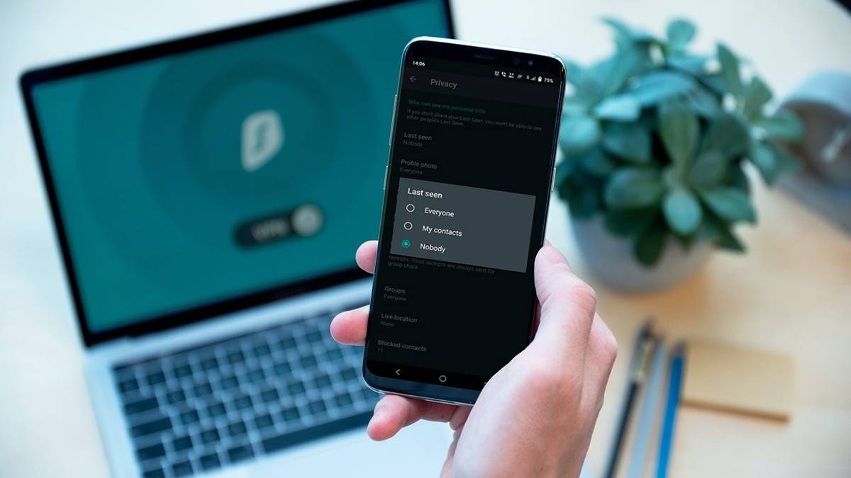 WhatsApp Last Seen settings open on smartphone in hand with laptop and plant in background