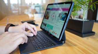 Two hands typing on a Magic Keyboard attached to an iPad Air 5 (2022) sitting on a table