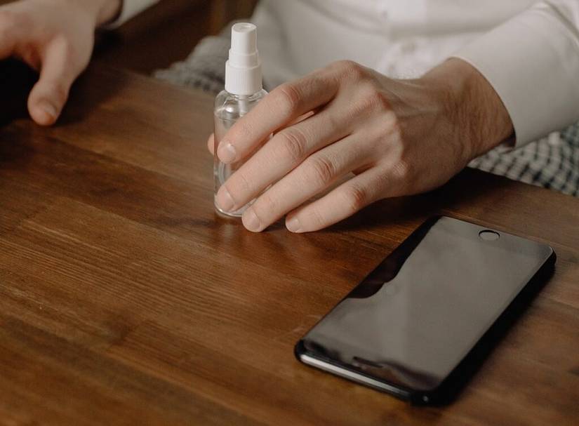 man holding spray bottle of home made screen cleaner next to mobile phone
