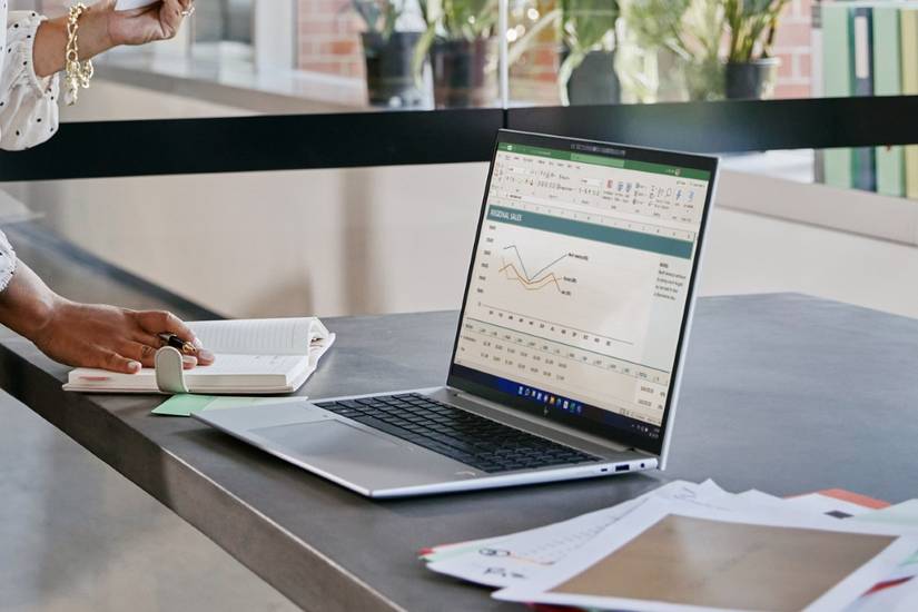 Angled view of the HP EliteBook 860 G9 on a desk next to documents and a notebook