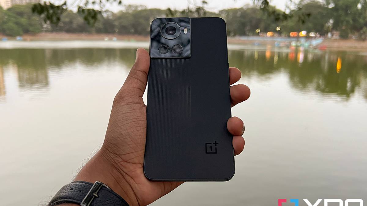 OnePlus 10R smartphone held out in hand, hand stretched out over a lake as the backdrop