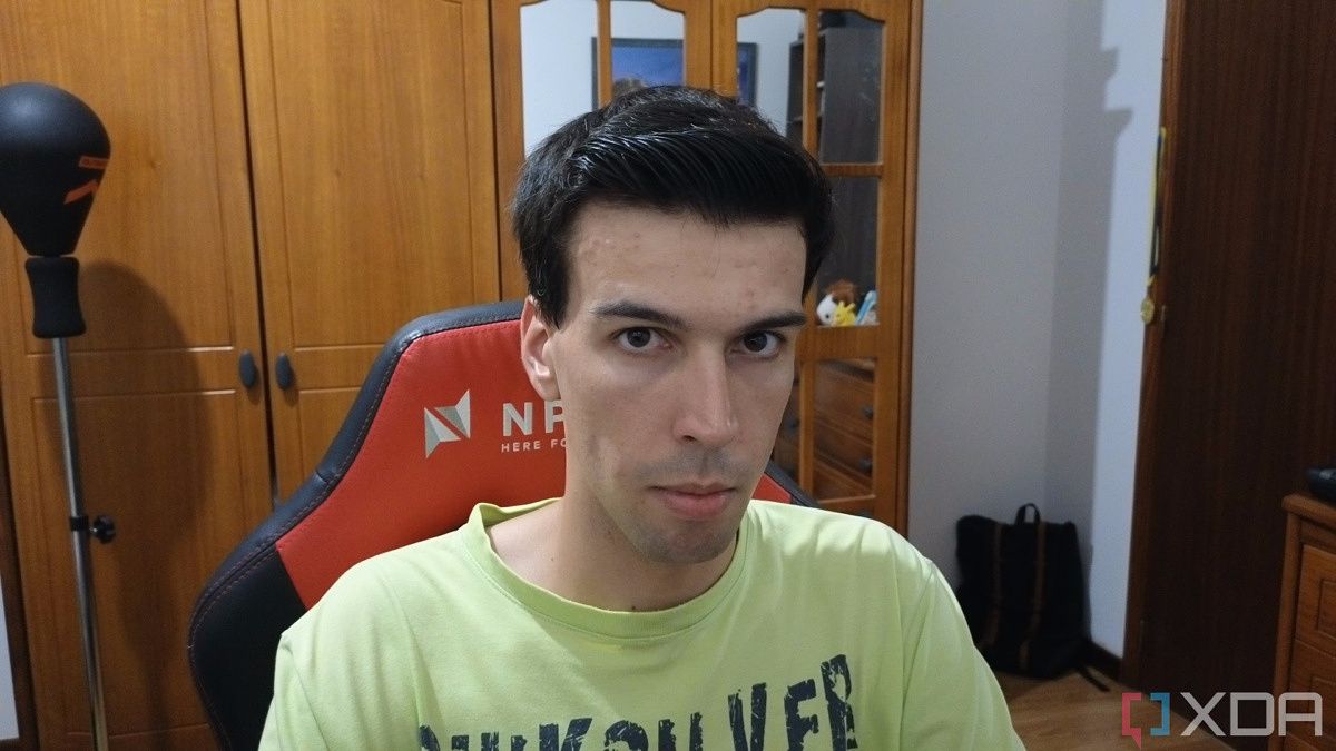 A picture of a man sitting on a chair with furniture behind him. The picture was taken with the Insta360 Link webcam with the HDR feature disabled