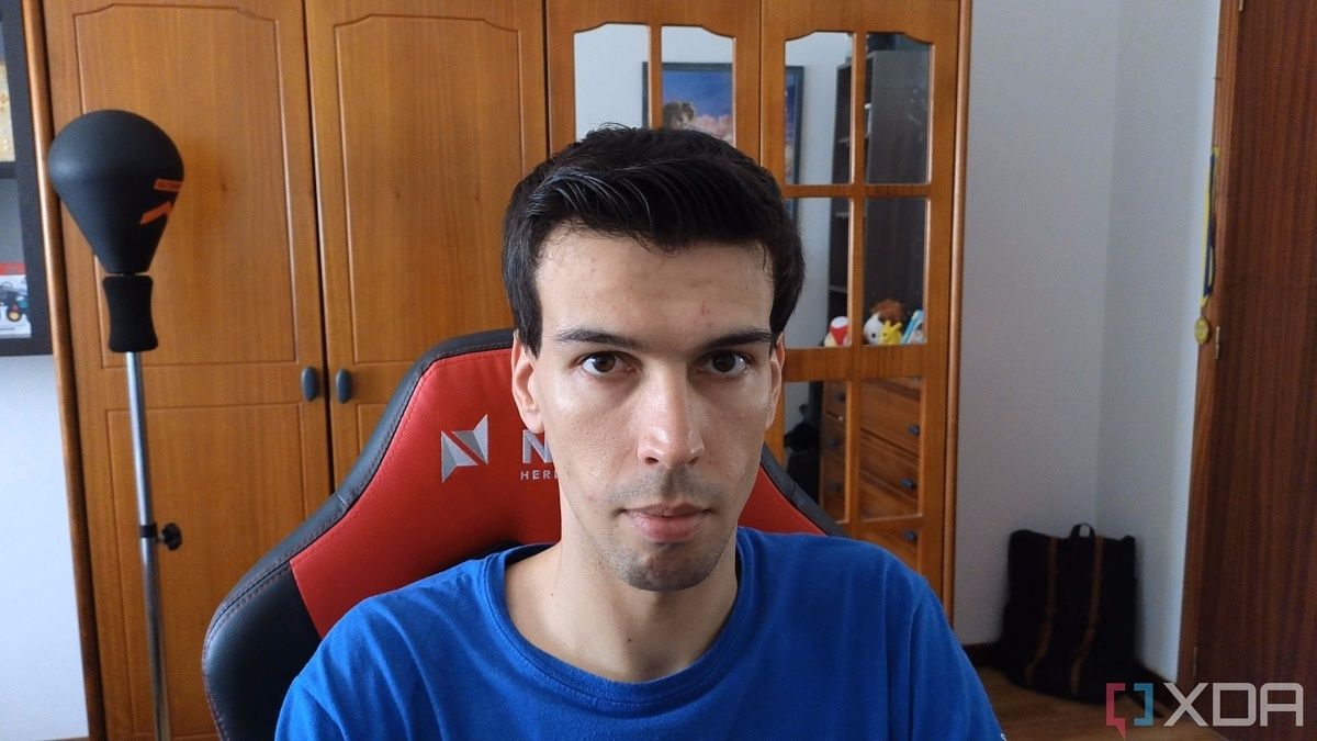 A picture of a man sitting on a chair with a wardrobe in the background. The picture was taken with the Insta360 Link webcam