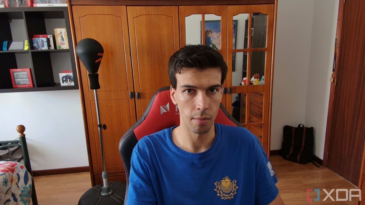 A picture of a man sitting on a chair with a wardrobe in the background. The picture was taken with the Obsbot Tiny 4K webcam