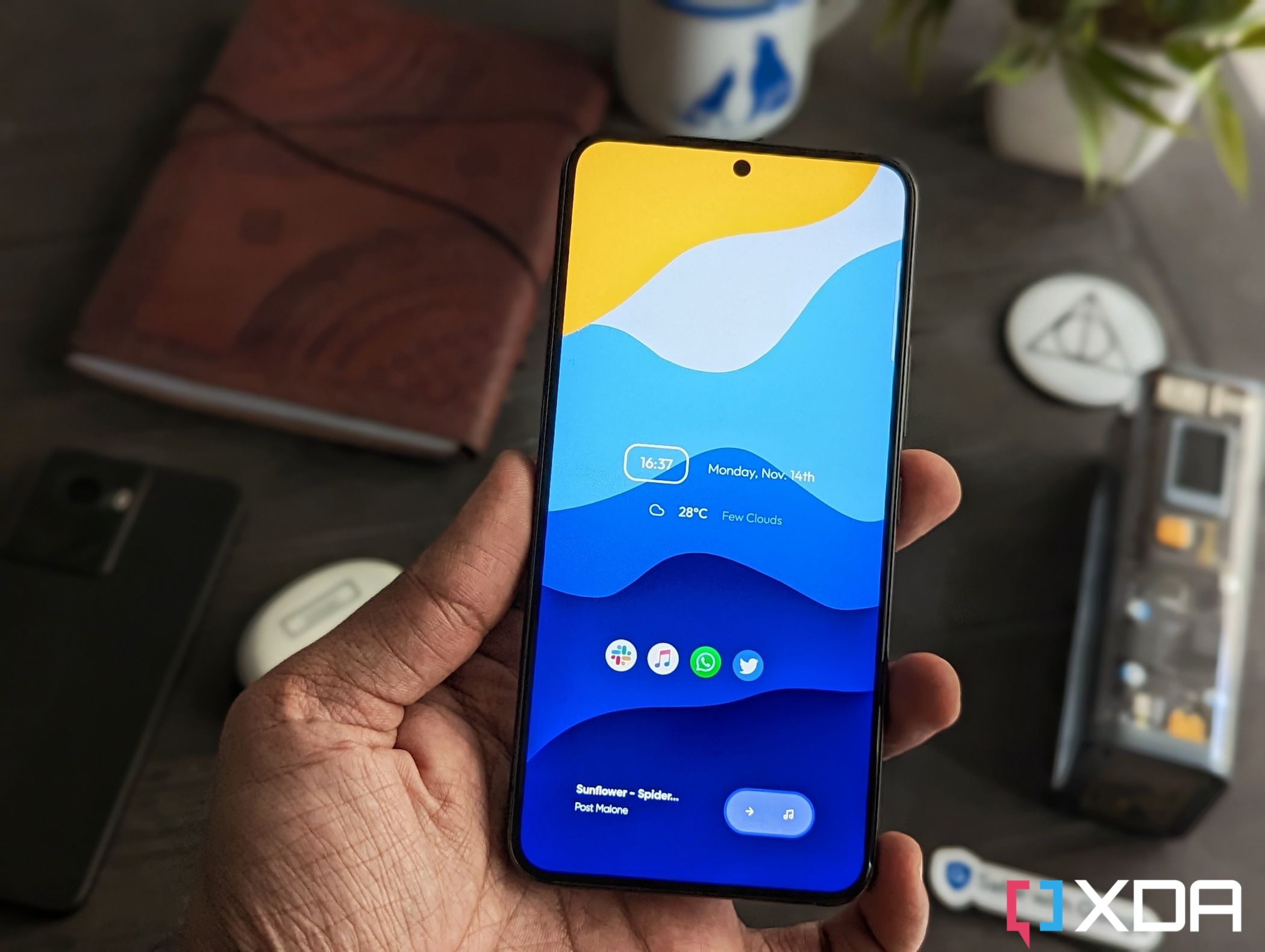An image showing a person holding the Samsung galaxy S22 in hand with a bunch of miscellaneous items in the background over a wooden table.
