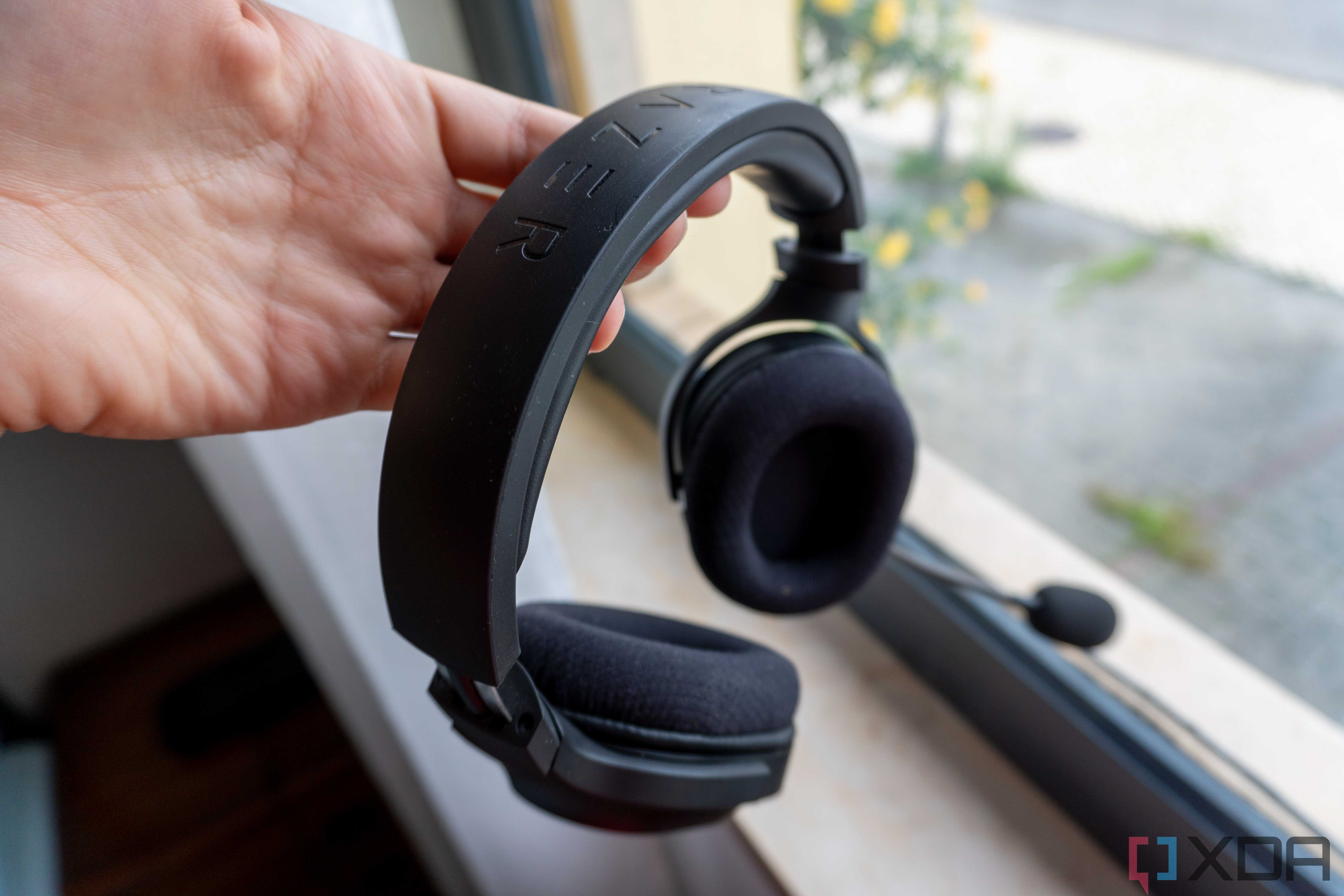 A Razer Barracuda X headset held on a person's hand by the headband, with a window in the background