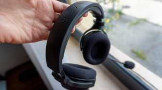A Razer Barracuda X headset held on a person's hand by the headband, with a window in the background