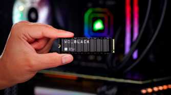 A person holding the WD Black SN850X gaming ssd with their thumb and the index finger with a gaming PC with RGB lights in the background.