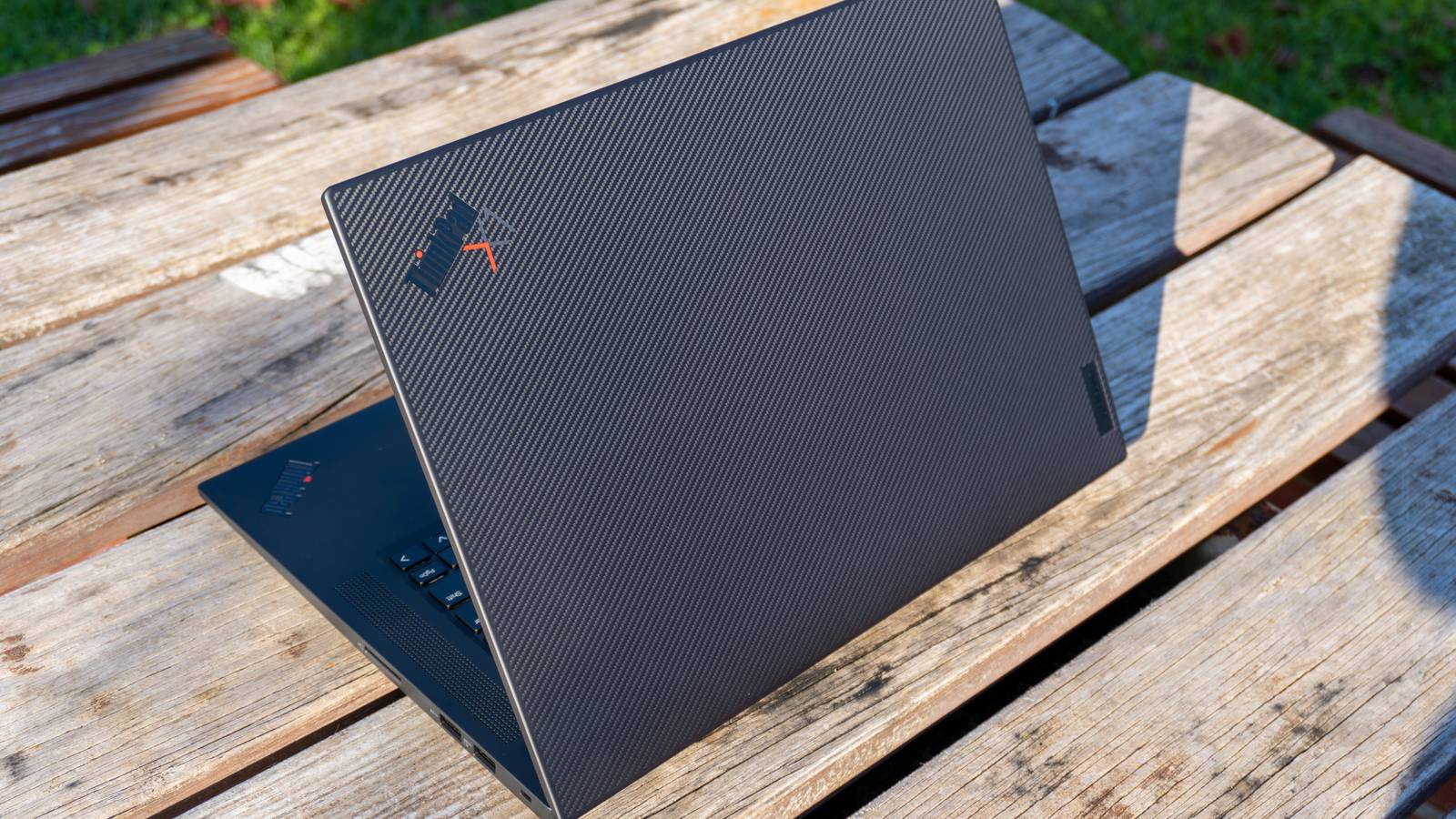 A Lenovo ThinkPad X1 Extreme Gen 5 laptop seen from behind at a left-side angle, with a carbon fiber pattern on the lid and a ThinkPad X1 logo in the top left corner