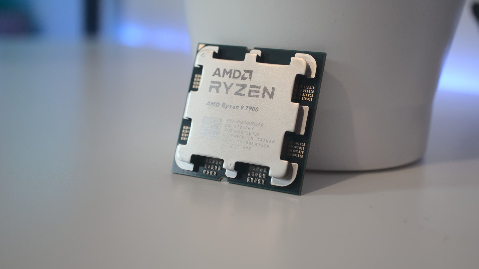 AMD Ryzen 9 7900 processor resting against a white container on a white desk