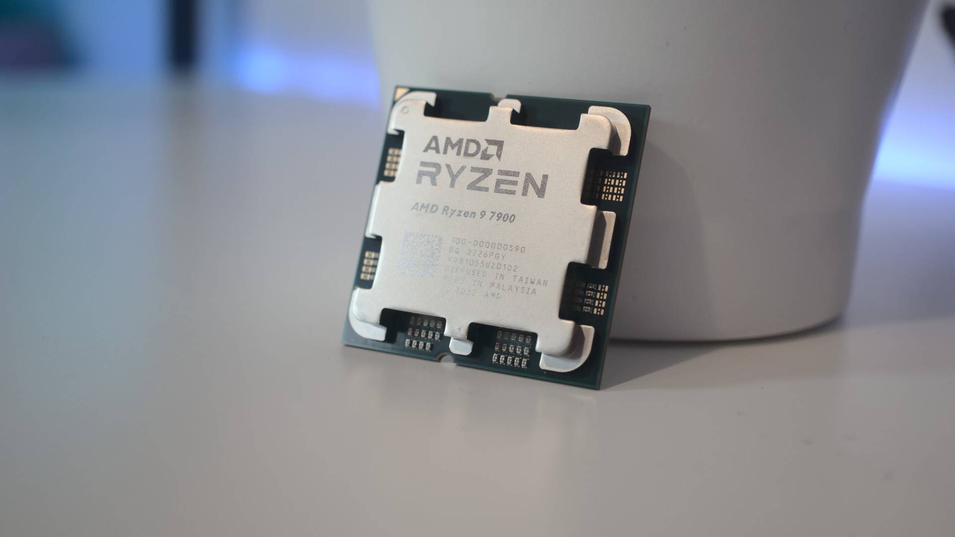 AMD Ryzen 9 7900 processor resting against a white container on a white desk