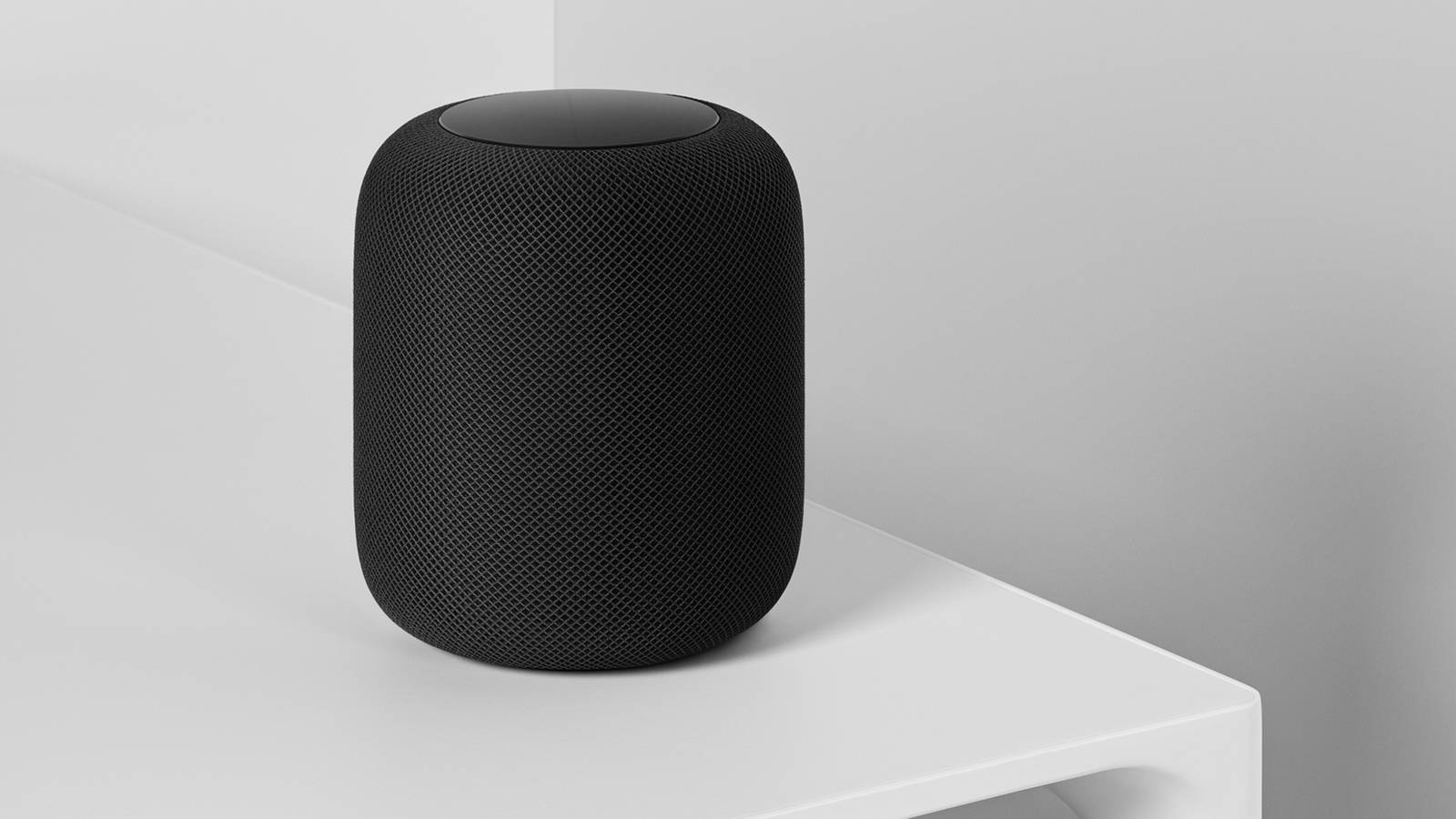 Black Apple HomePod on white table with white walls in the background.