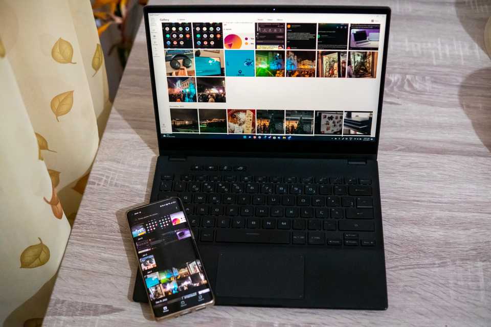 A laptop with a smartphone resting on the keyboard base. The two devices are displaying a gallery with the same photos using the Intel Unison app.