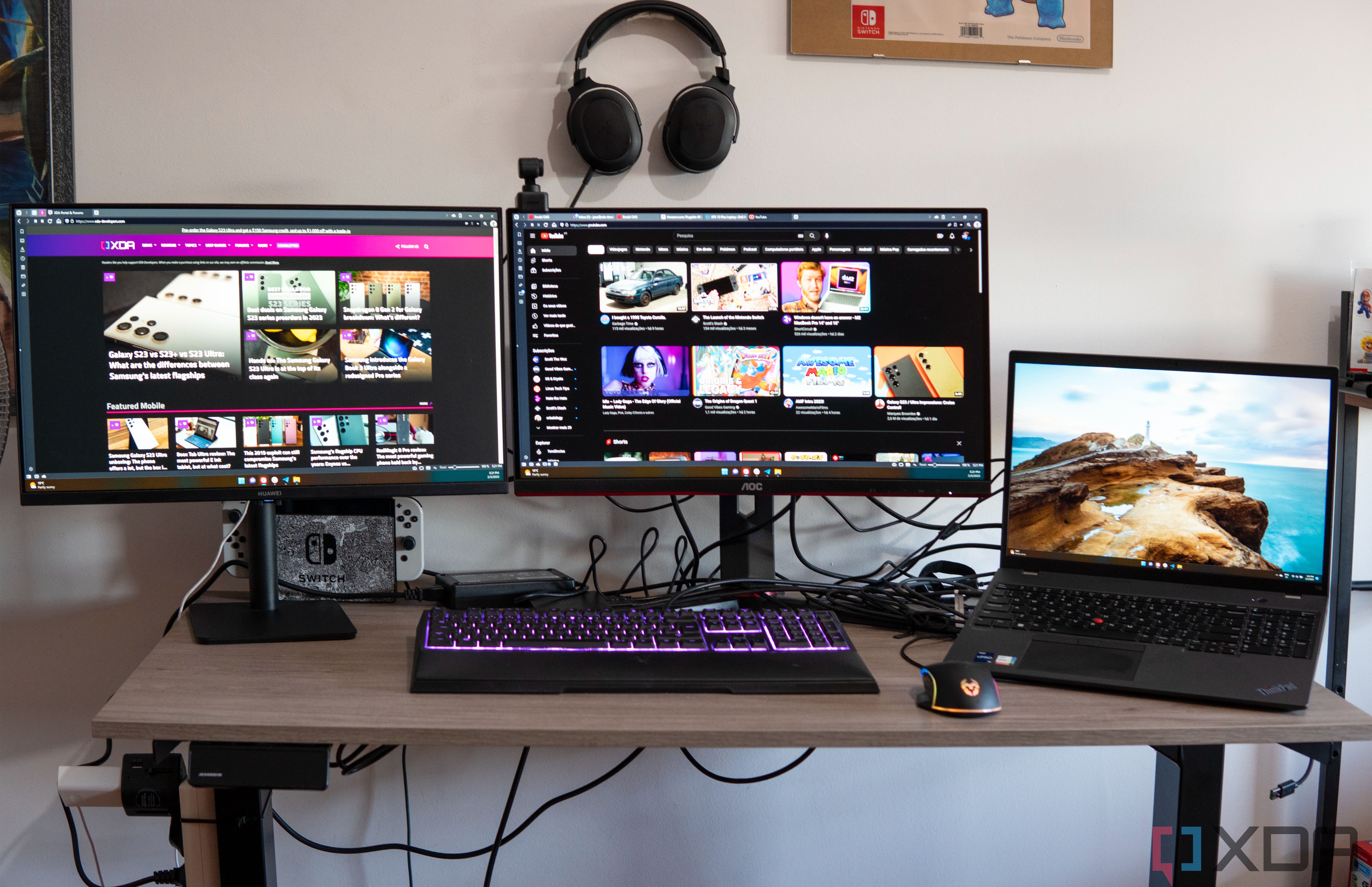 A laptop, two monitors, and various computer accessories on a table