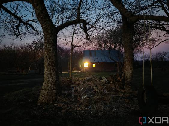 Photo of a barn with a light on inside at night through trees