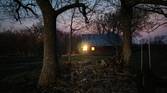 Photo of a barn with a light on inside at night through trees