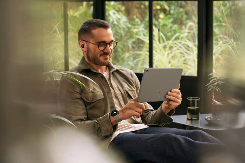 An image showing a person using a Hazel-colored Pixel Tablet while wearing a Pixel Watch and Pixel Buds.