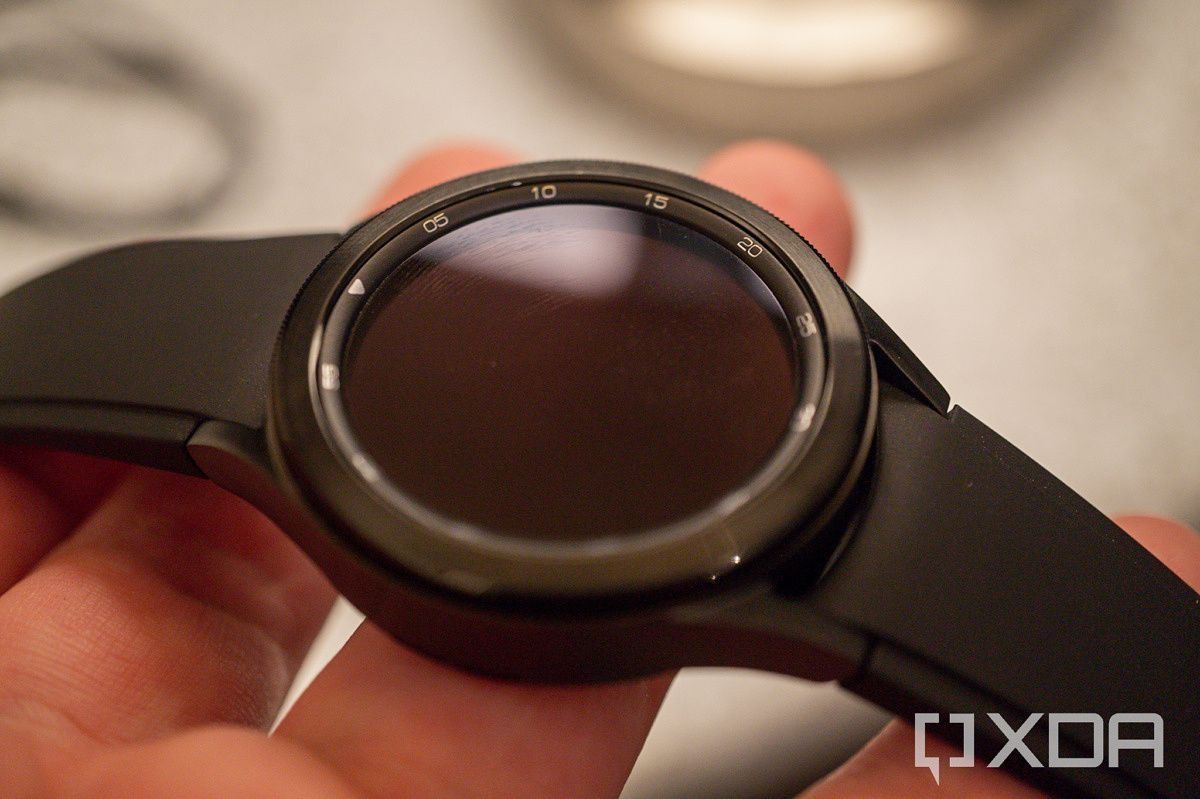 A Samsung Galaxy Watch 4 Classic held in someone's fingers