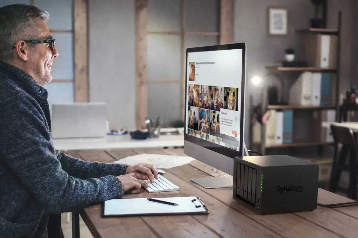 Synology diskstation 1522 plus network attached storage on a desk next to a man working on a computer