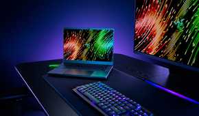 A Razer Blade 14 on a desk next to computer peripherals, including a monitor and keyboard.