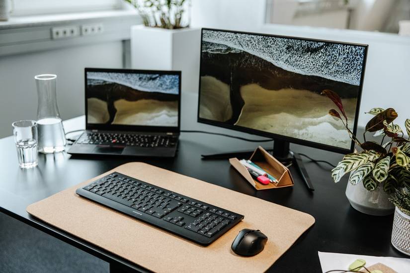 Black keyboard next to a mouse in front of a desktop monitor and a laptop on a desk
