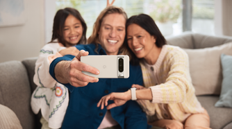 A person holding the Pixel 8 Pro horizontally to take a group selfie with two others in the frame.