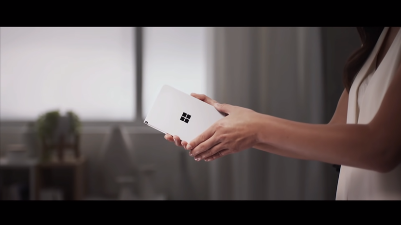 Woman holding a Surface Duo fully closed with the Microsoft logo visible