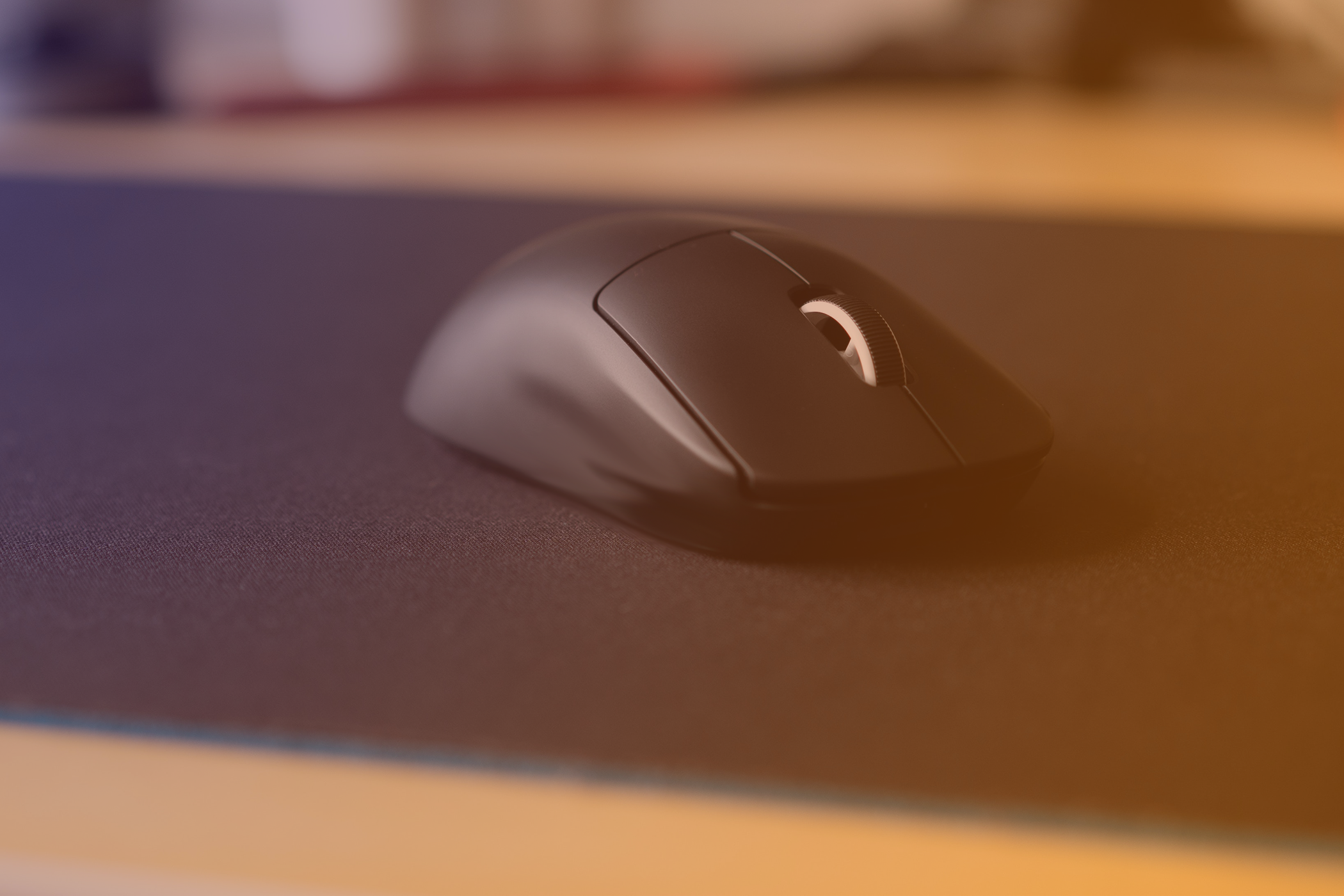 A gaming mouse on a large gaming mouse pad with a purple to orange hue