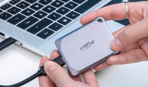 Crucial X9 Pro 1TB Portable SSD in hand next to computer