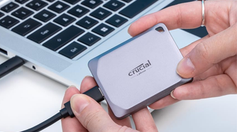 Crucial X9 Pro 1TB Portable SSD in hand next to computer