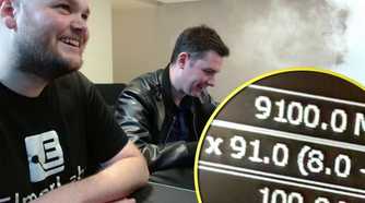 Two men sit at a desk smiling, with 9100MHz showing on a magnified screenshot at a corner