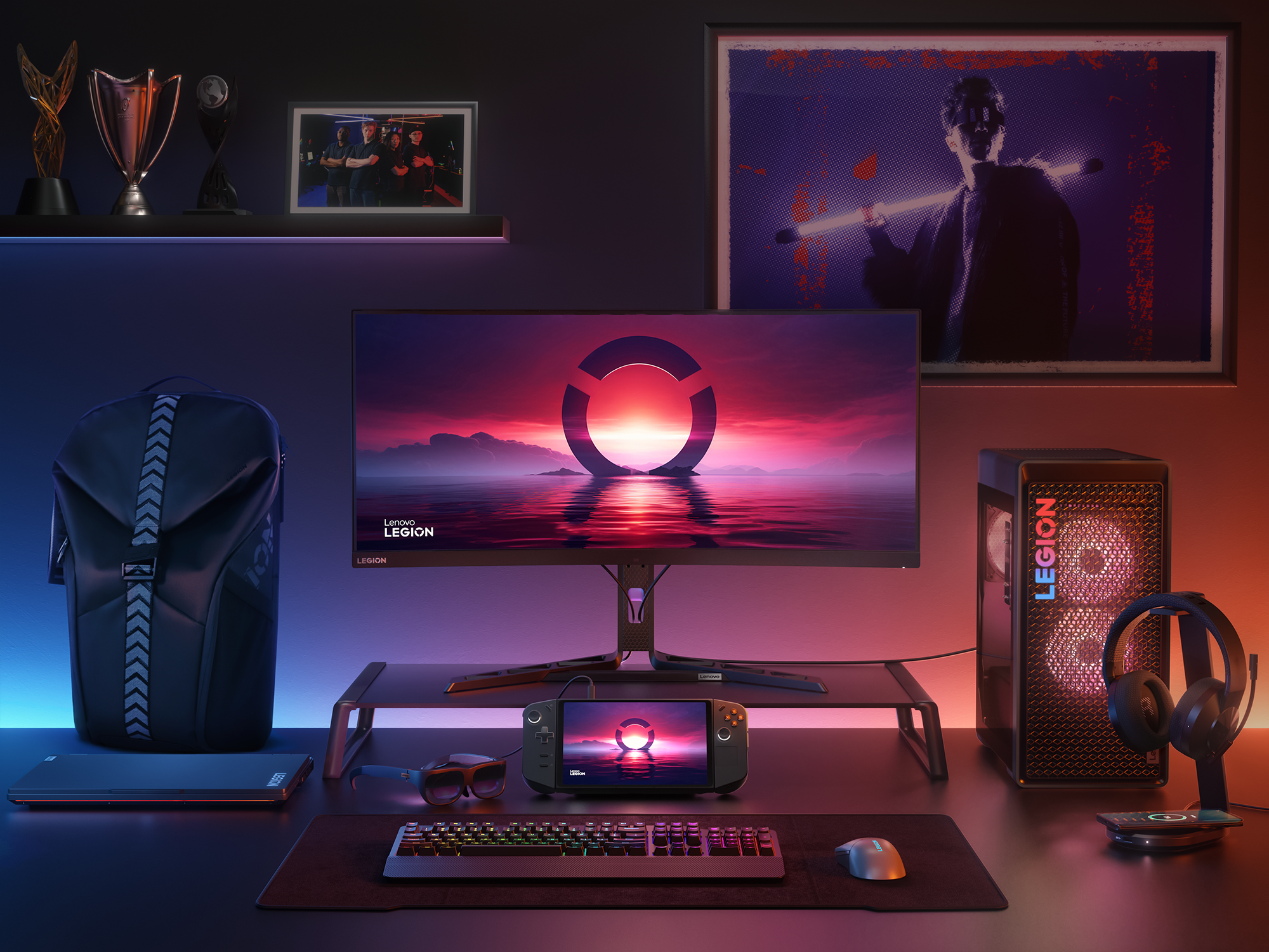 A full Lenovo computer setup to the right, custom RGB backlighting desktop with wallpapers on the wall, a Lenovo laptop to the left, and the Legion Go is in the middle under the computer monitor