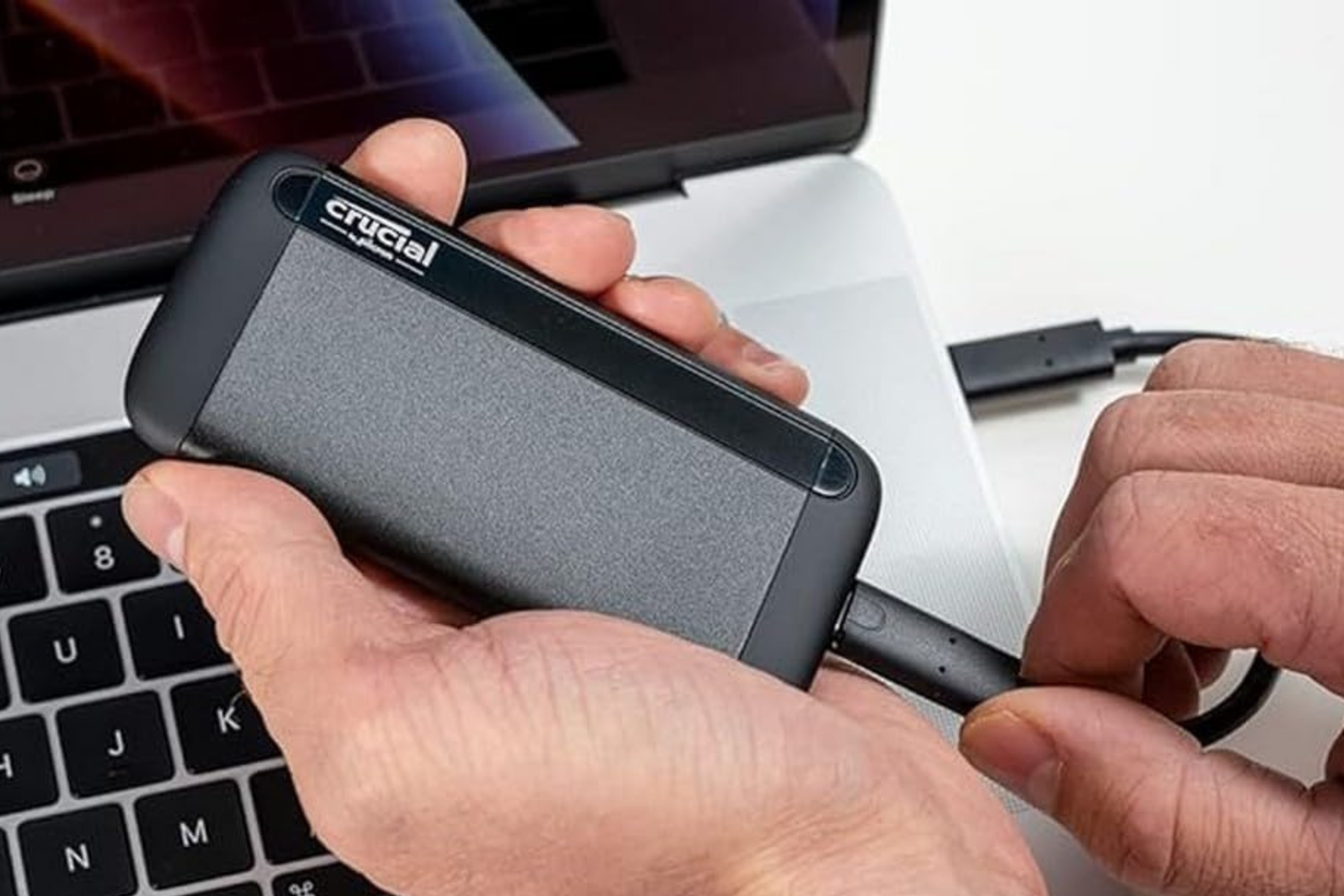 Crucial X8 Portable SSD in hand being plugged into computer