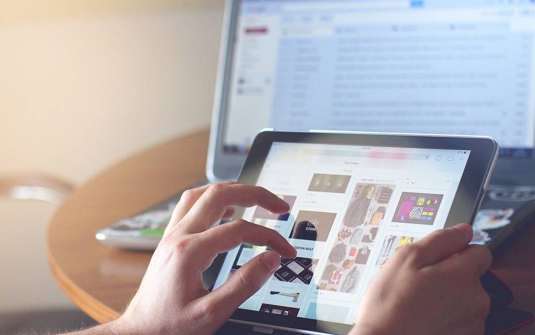 hands using tablet with laptop in the background