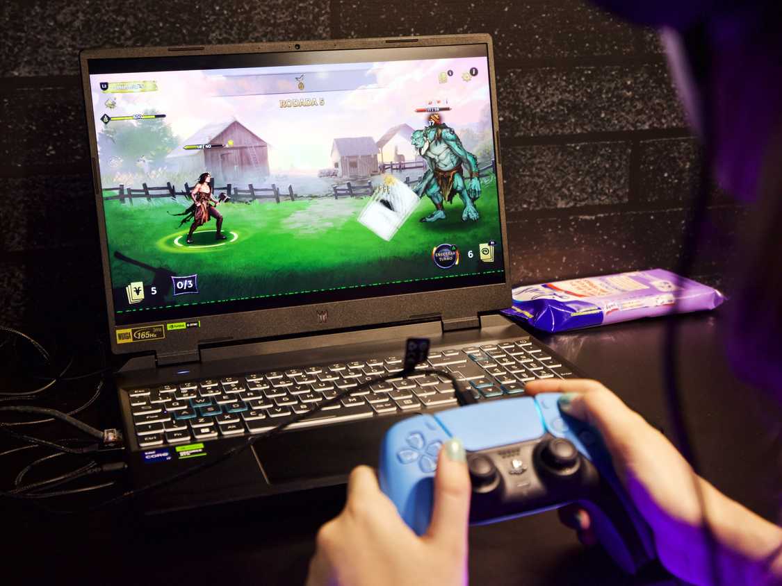 person holding playstation controller while playing video game on a laptop computer