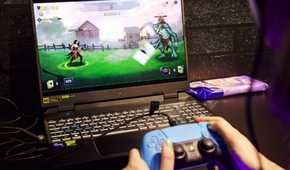person holding playstation controller while playing video game on a laptop computer
