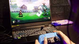 person holding playstation controller while playing video game on a laptop computer