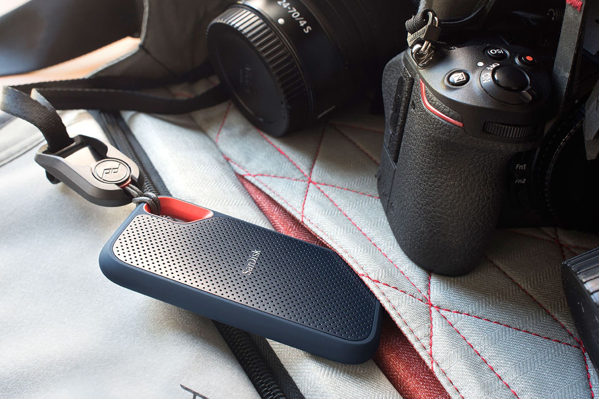 SanDisk Extreme Portable SSD attached with a lanyard to a bag next to a camera