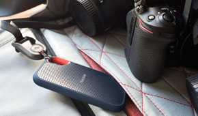 SanDisk Extreme Portable SSD attached with a lanyard to a bag next to a camera