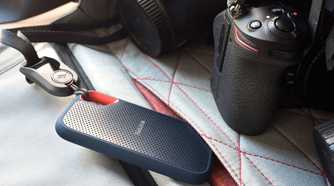 SanDisk Extreme Portable SSD attached with a lanyard to a bag next to a camera