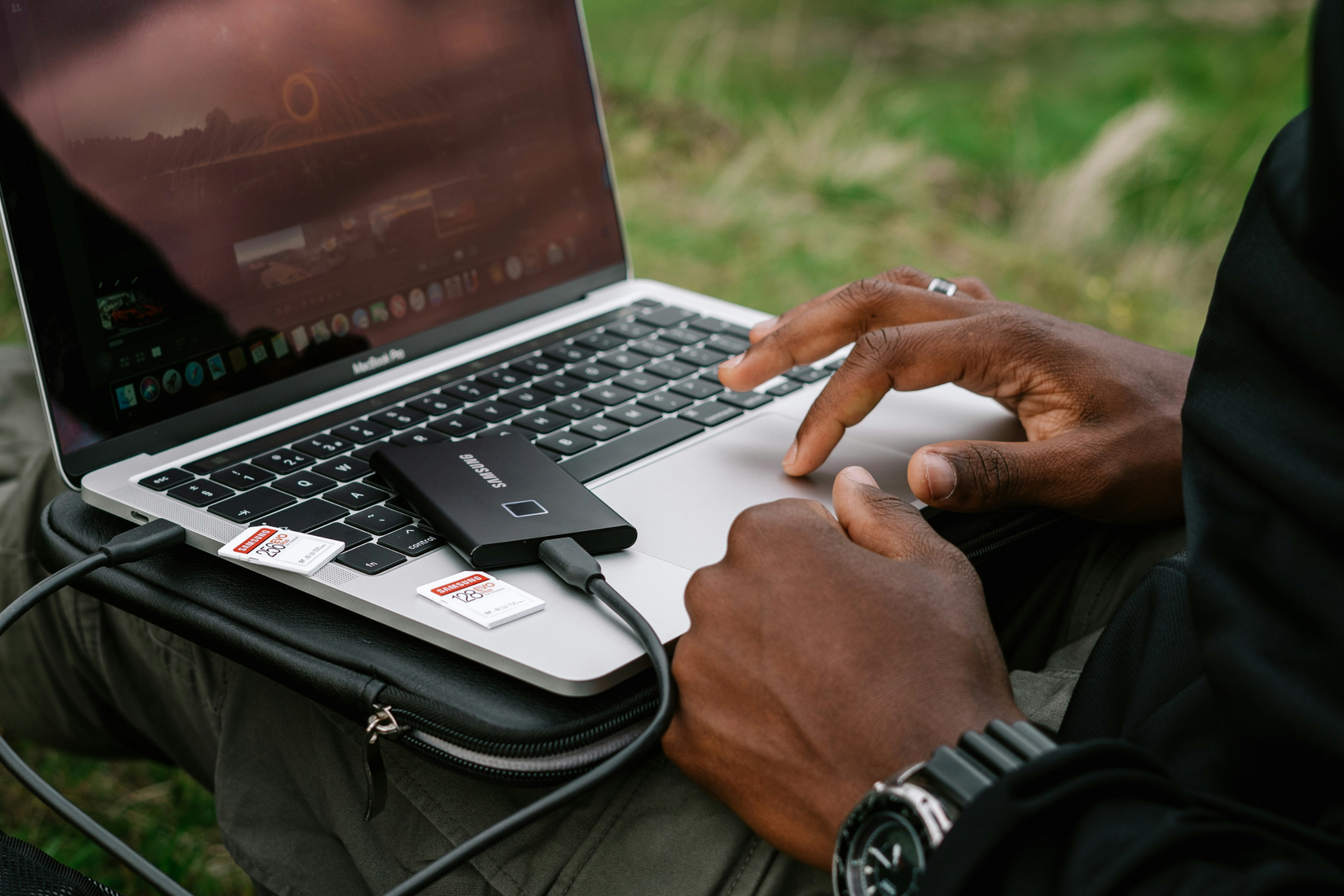 A man using his laptops touchpad with an external SSD plugged in and two SD cards next to it