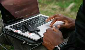 A man using his laptops touchpad with an external SSD plugged in and two SD cards next to it