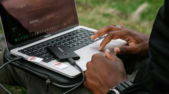 A man using his laptops touchpad with an external SSD plugged in and two SD cards next to it