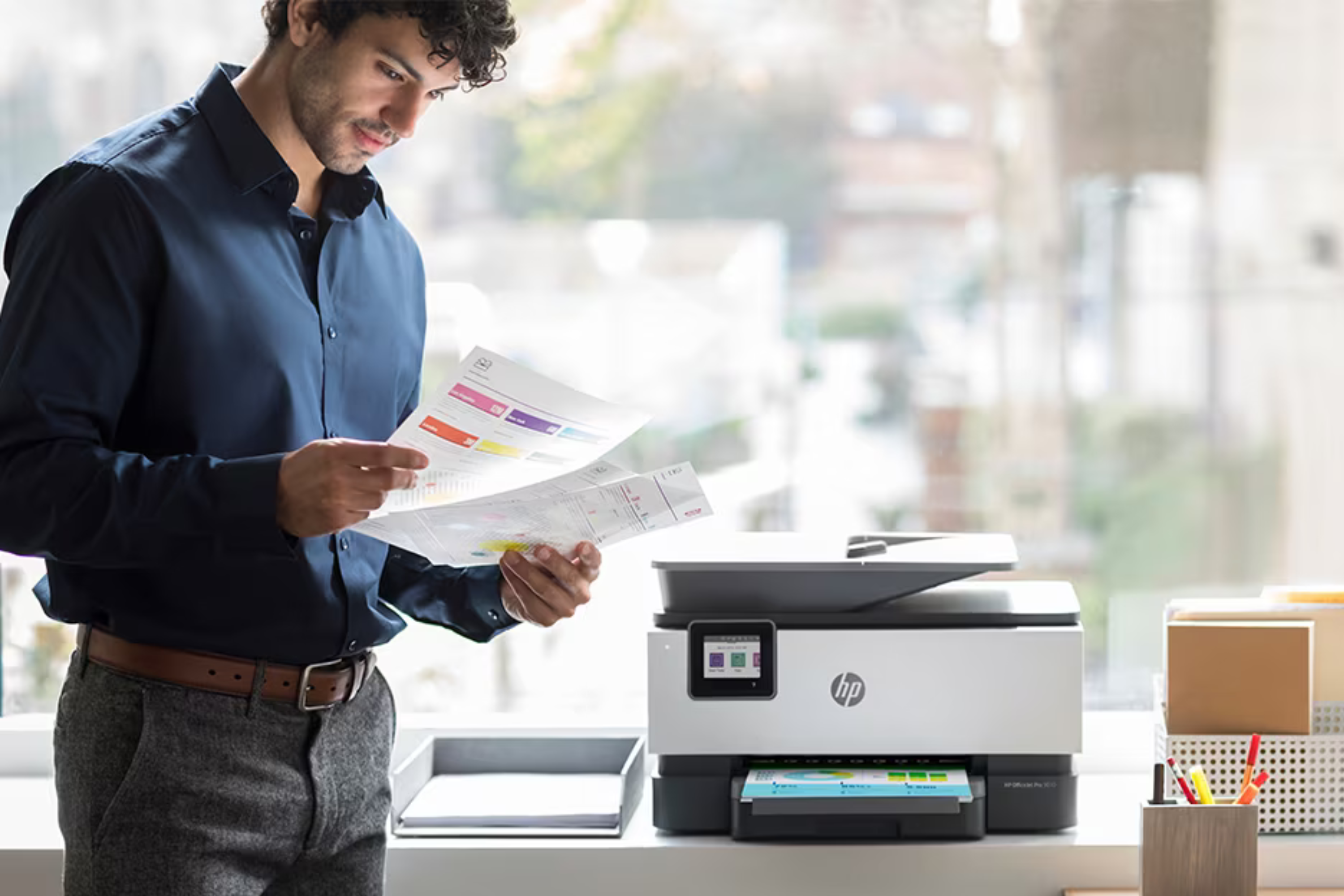 person next to HP printer holding recently printed documents 