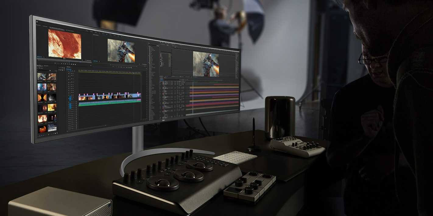 An LG UltraWide 49WQ95C monitor on a desk next to mixing tools used for editing video professionally