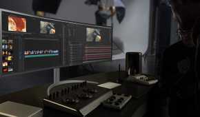 An LG UltraWide 49WQ95C monitor on a desk next to mixing tools used for editing video professionally